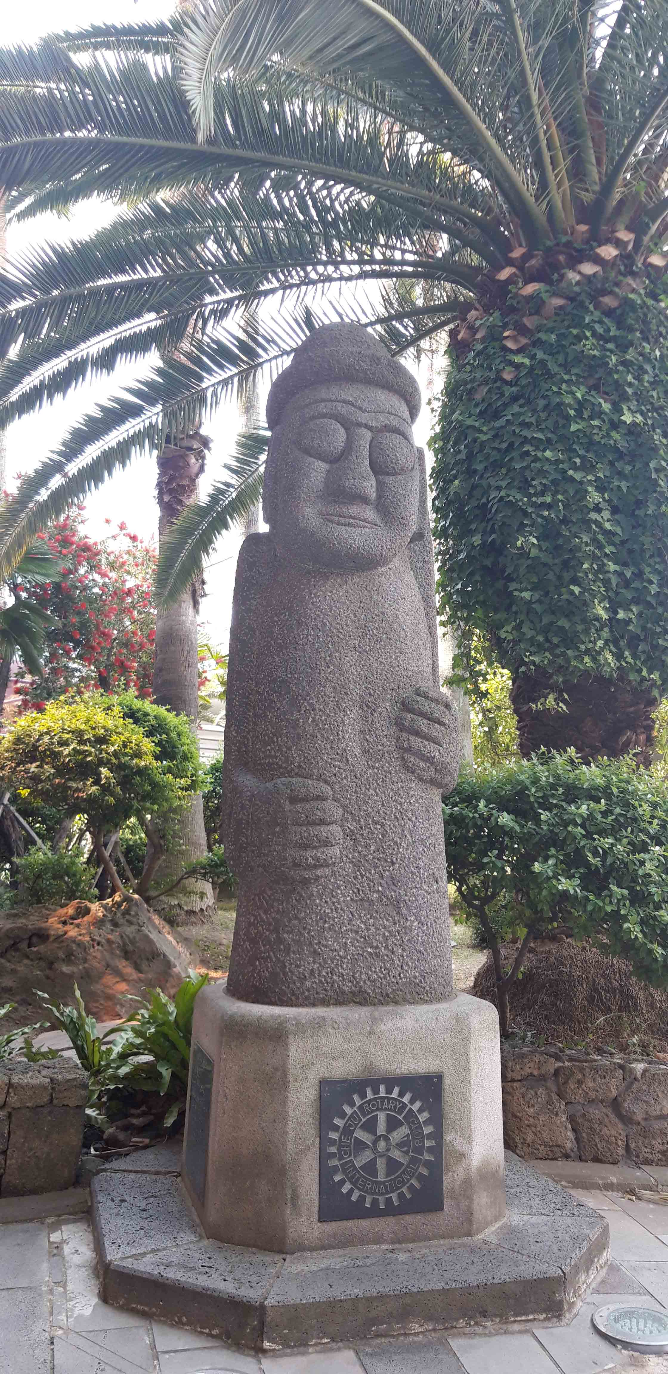 제주공항에 서 있는 하르방. 뒤에 야자수가 보인다.  