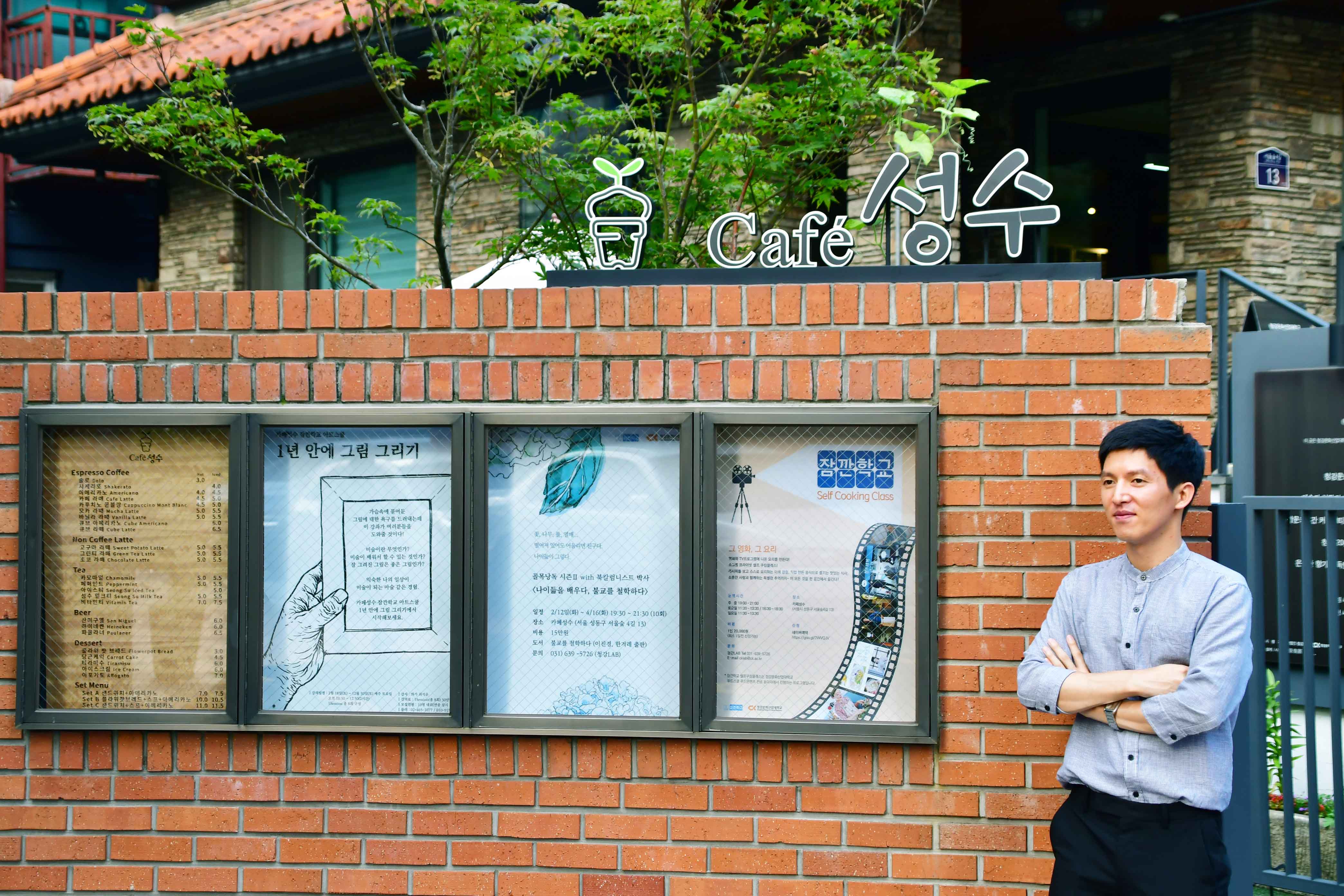 카페 앞에서 포즈를 취하는 이상국 작가 / 간판 문구 : cafe 성수 / 포스터 문구 : 1년 안에 그림 그리기 잠깐학교 