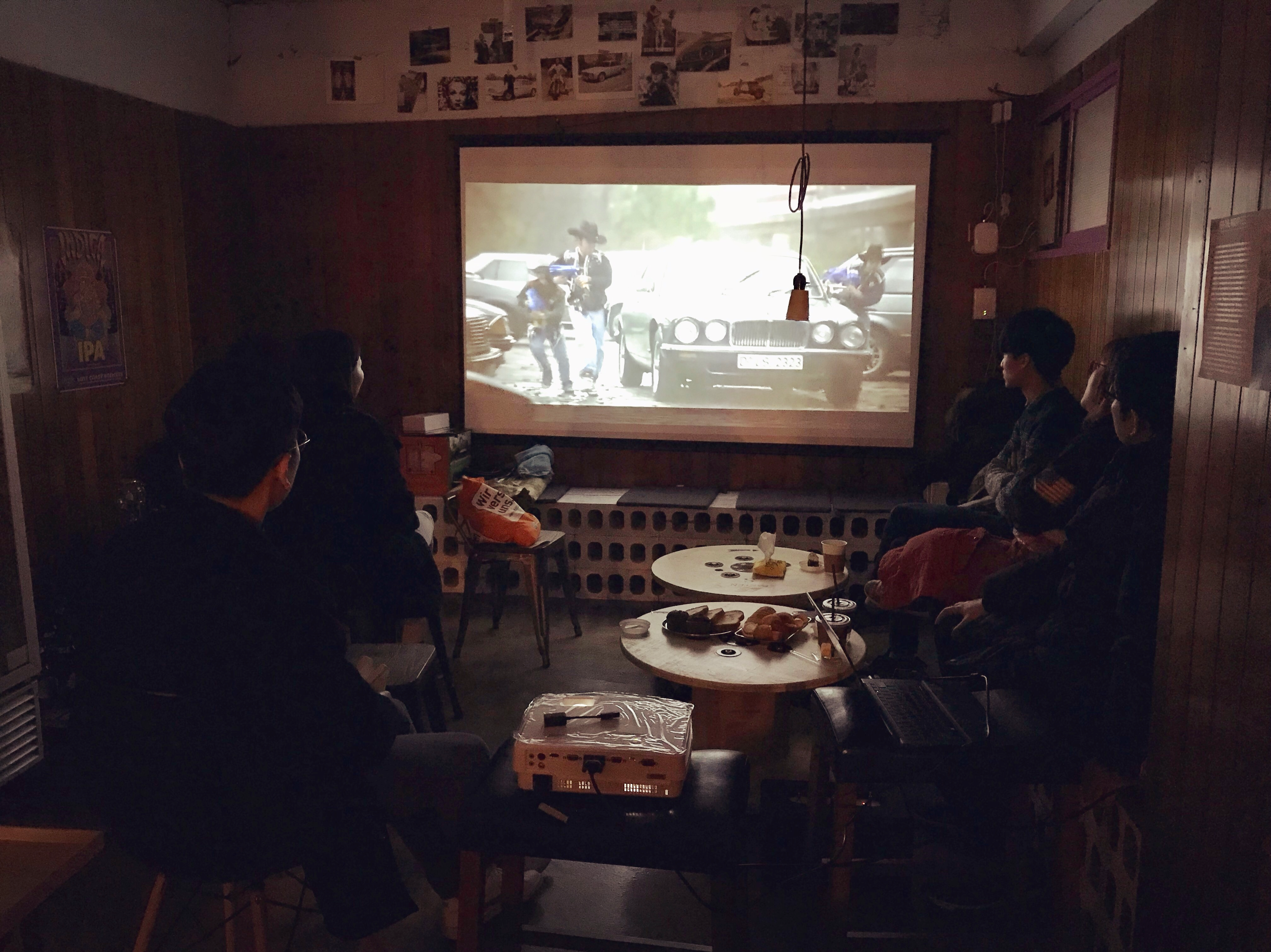 책방 속 비밀공간에 모여 앉아 스크린을 통해 영화를 보는 사람들
