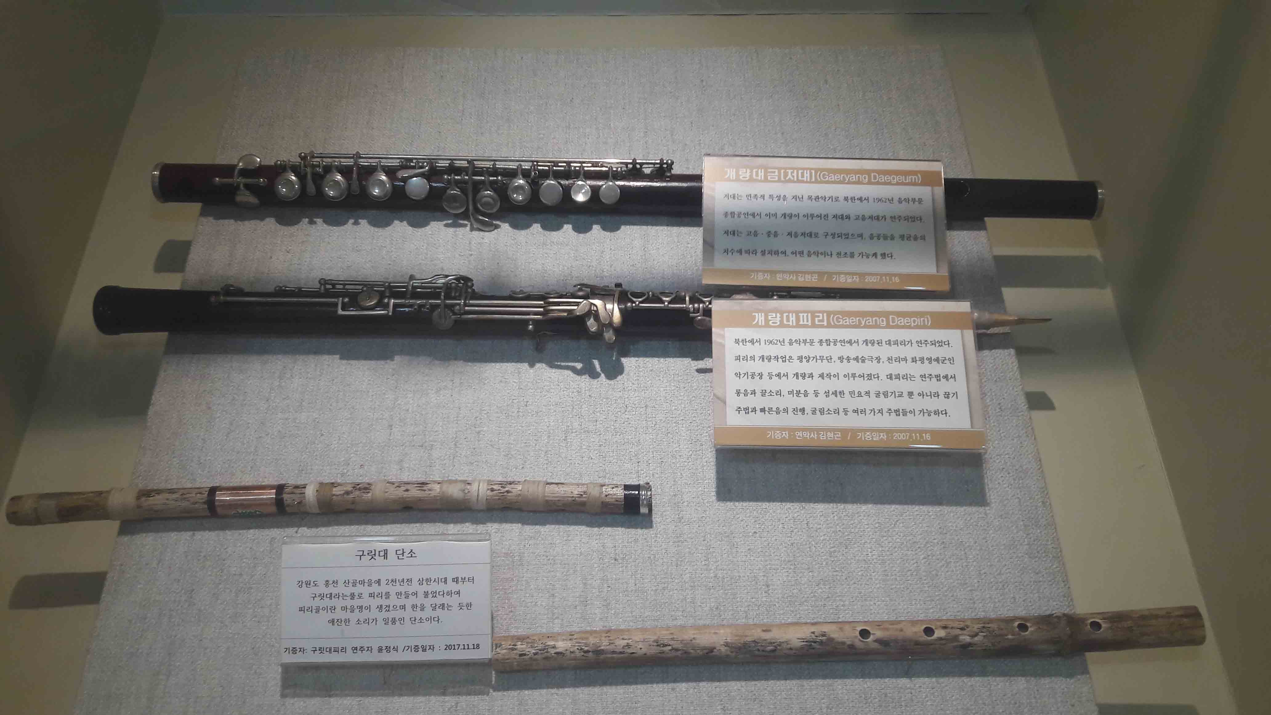 개량대금처대] (Gaeryang Daegeum) 기대는 민족 특성을 기닌 목관악기로 북한에서 1962년 음악부문 중공인에서 이미 개량이 이루어진 거대의 고음거대가 연주되었다. 기대는 고을 • 중음 · 거음 시대로 구성되었으며, 음주들을 평균을의 기수에 따라 실거하여, 어떤 음악이나 건조를 가는게 했다. 기증자 : 인악사 김원곤 / 기중일자 : 2007.11.16 | JH CH I 2) (Gaeryang Daepiri) 북한에서 1962년 음악부문 종합공연에서 개량된 대피리가 연주되었다. 피리의 개량작업은 평양가무단, 방송예술극장, 천리마 화평영예군인 악기공장 등에서 개량과 게작이 이루어졌다. 대피리는 연주법에서 롱음과 끌소리, 미분음 등 섬세한 민요적 굴림기교 뿐 아니라 끊기 주법과 다른음의 진행, 굴림소리 등 여러 가지 주법들이 가능하다. 기증자 : 연악사 김현곤 | 기증일자 : 2007.11.16 | 구릿대 단소 강원도 홍천 산골마을에 2천년전 삼한시대 때부터 | 구릿대라는풀로 피리를 만들어 불었다하여 피리골이란 마을명이 생겼으며 한을 달래는 듯한 | 애잔한 소리가 일품인 단소이다. 기증자: 구릿대피리 연주자 윤정식 기증일자 : 2017.11.18